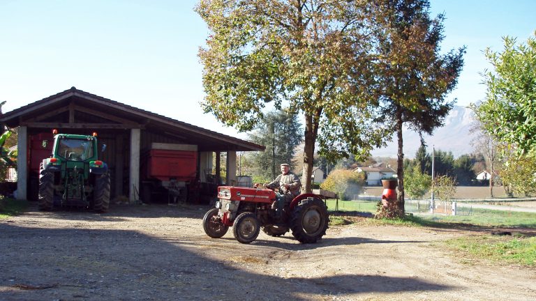 Agriculteur au volant d'un tracteur devant une grange, montagnes en arrière-plan