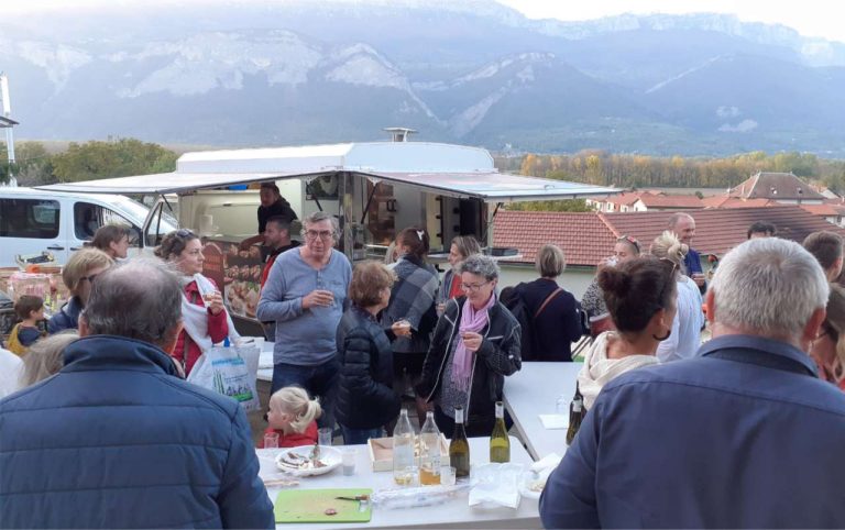 Habitants réunis autour d'un camion de restauration lors d'un apéro marché, vue sur les montagnes