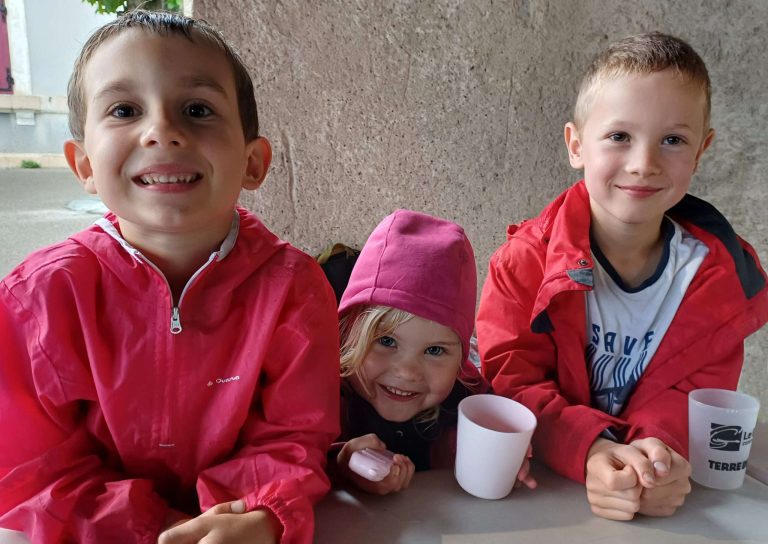 Trois enfants souriants avec des gobelets, lors d'un événement communal